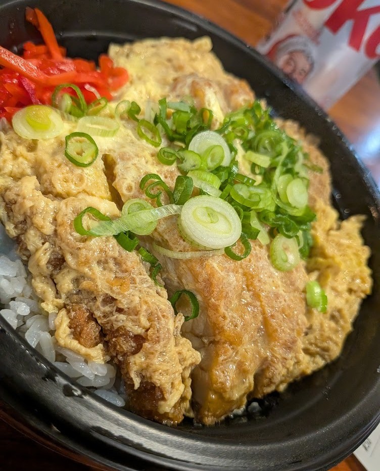 A bowl of fried food, sliced herbs, and red peppers.