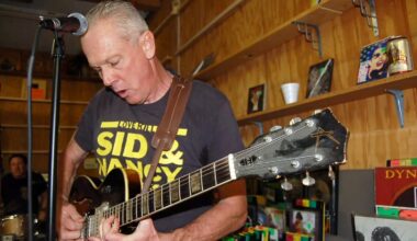 A white-haired punk guitarist plays in a record store.
