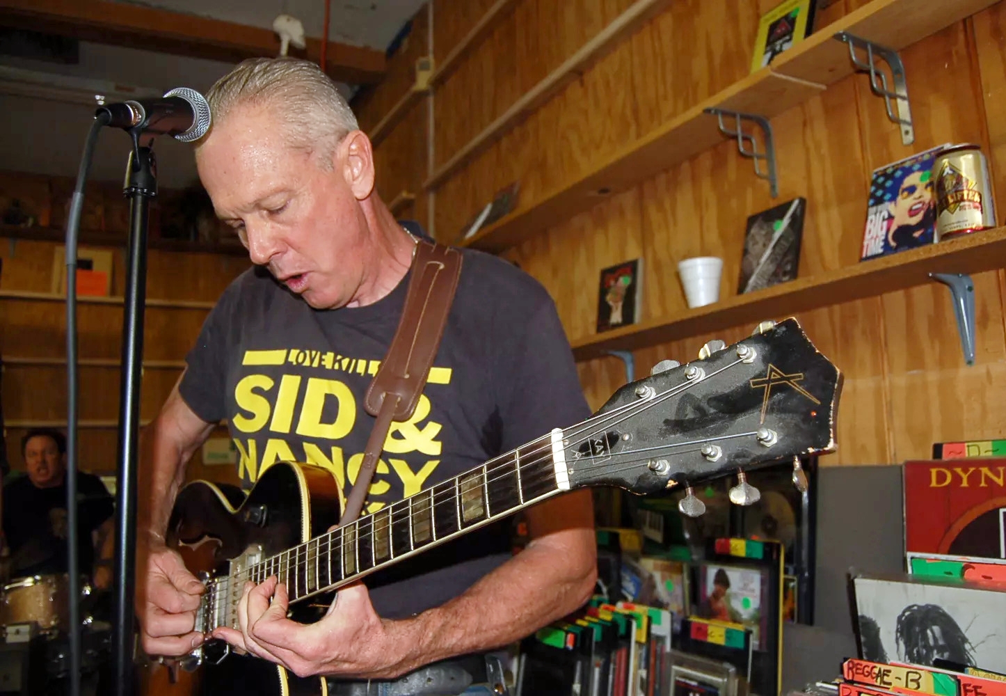 A white-haired punk guitarist plays in a record store.