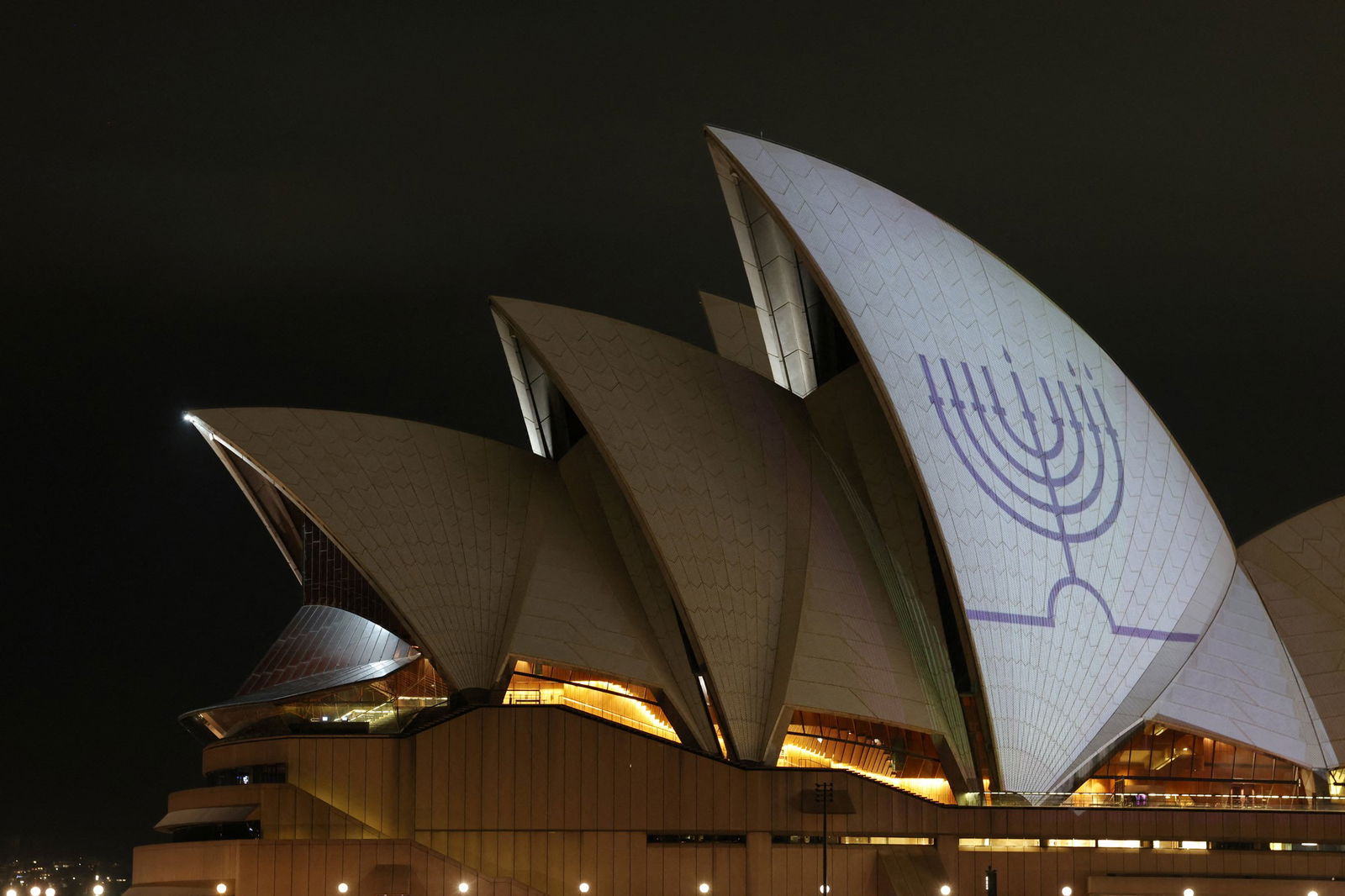 A white roof of the Sydney Opera House is lit up white with a blue menorah