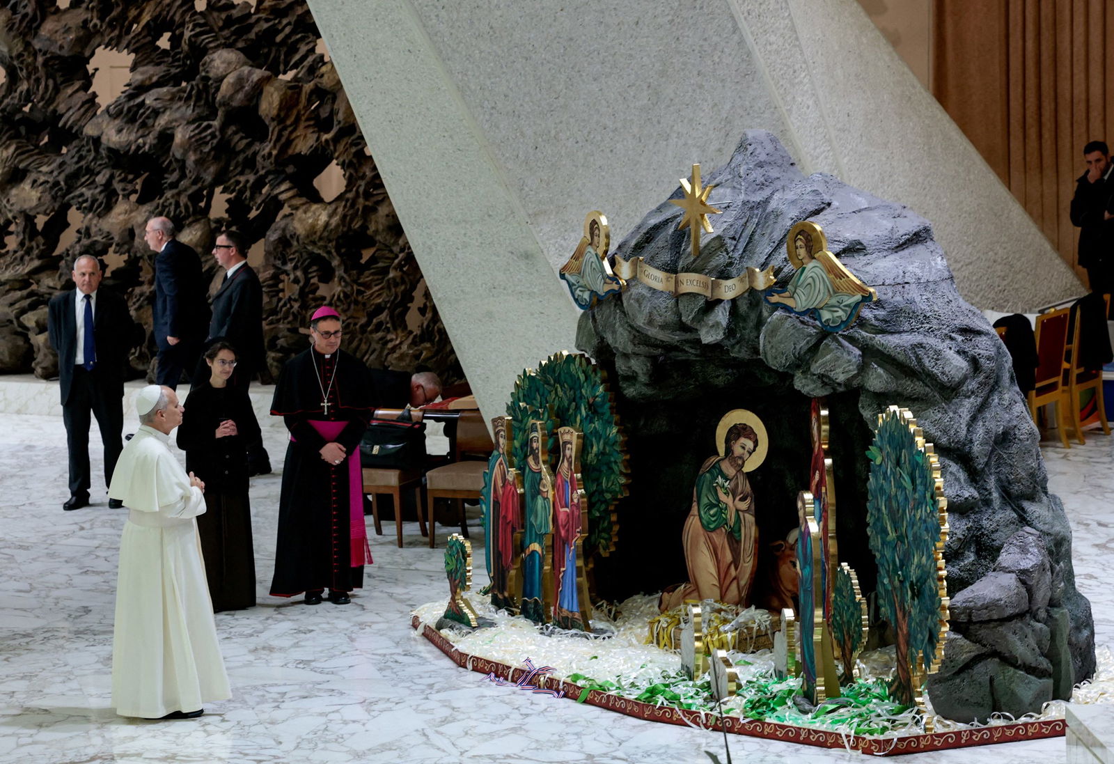 A man in a regal white gown and hat looks at a large nativity scene