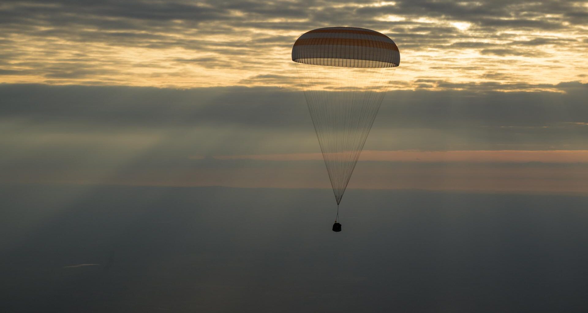 The photo features a dim horizon with the Soyuz MS-26 spacecraft as it lands by parachute.