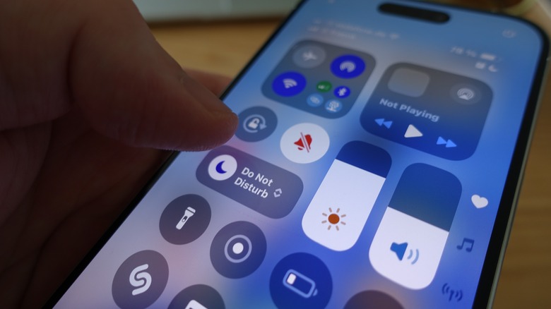iPhone's Control Center with person's thumb reaching for do not disturb toggle