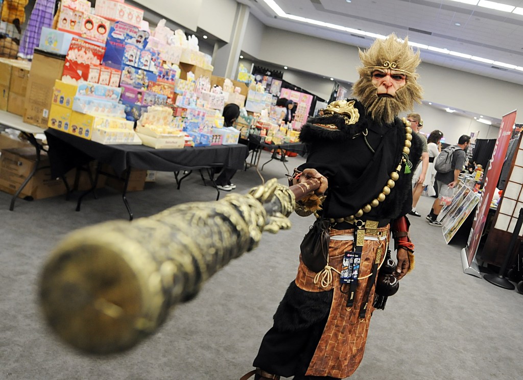 A man in a monkey costume points a staff at the camera.