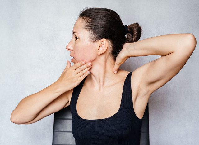A woman gently rotates her head with both hands while doing the McKenzie method exercise for the neck, neck pain relief exercises