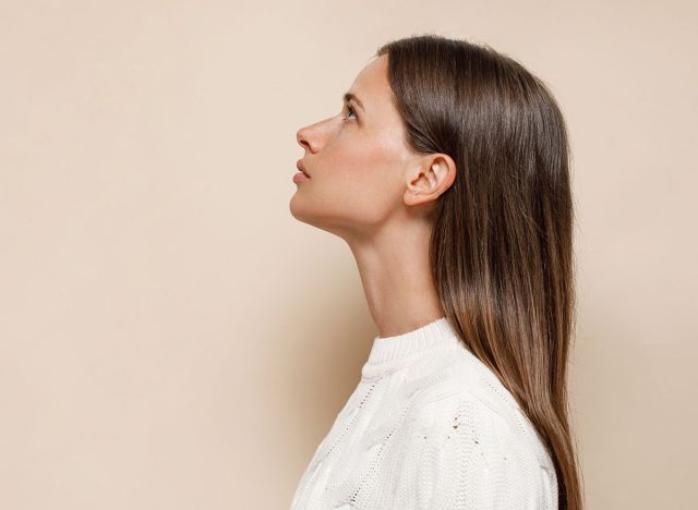 Caucasian female with long shiny hair with nude makeup in profile on a beige background