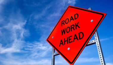 Bright orange road work ahead sign against a blue sky.