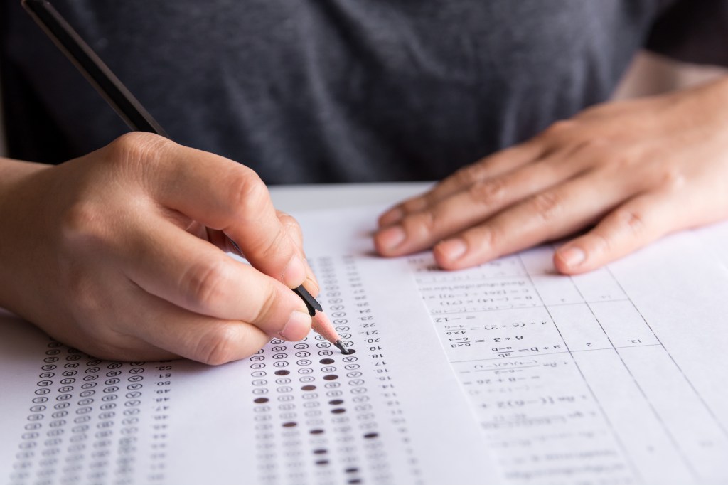 A student fills in a bubble on a multiple-choice exam answer sheet with a pencil.