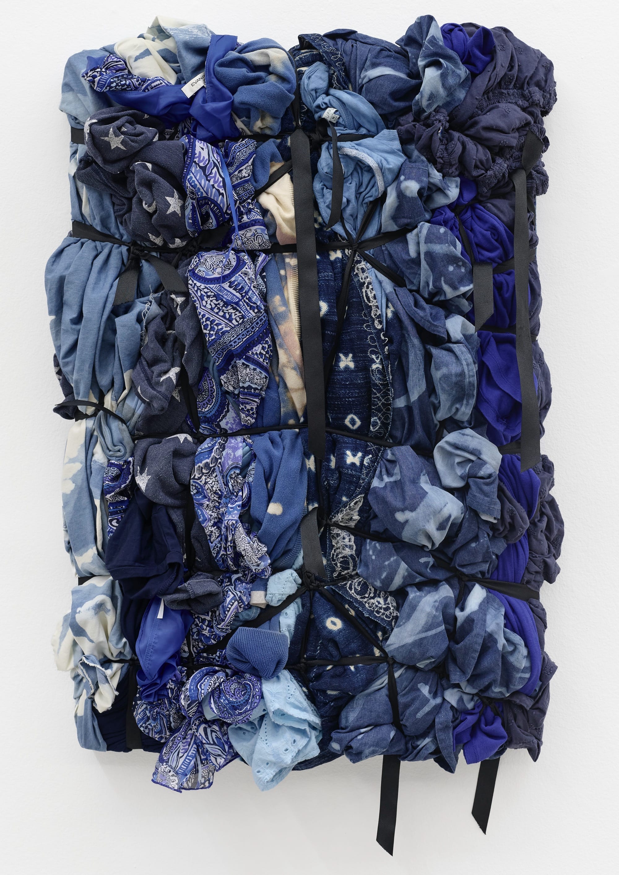 A soft wall sculpture by Shinique Smith of numerous bunched-up indigo-dyed fabrics and bandanas