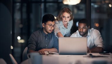 Three investors look at something on a laptop in a darkened office.