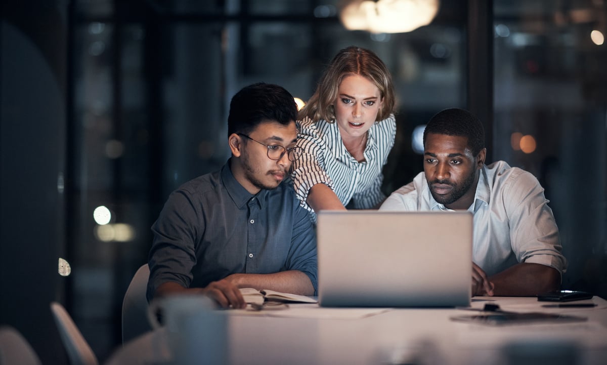 Three investors look at something on a laptop in a darkened office.