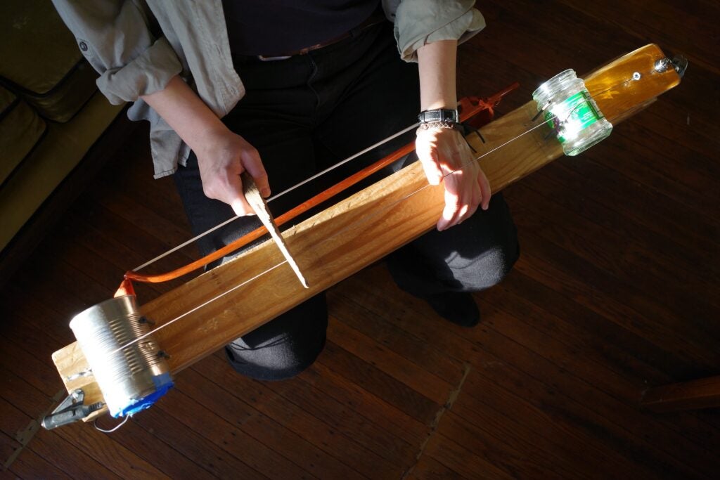 A person is playing a one-stringed musical instrument which is lying flat on their lap