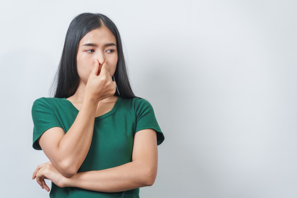 woman in green tshirt against a plain background holding her nose