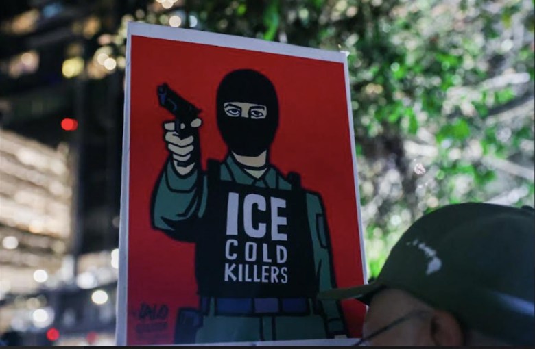 A sign held by a man in a cap shows an armed masked man on a red background. It reads, "ICE cold killers."