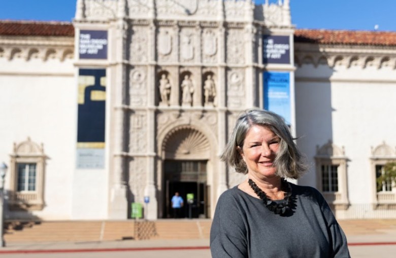 A woman stands on a plaza in front of the ornate facade of a building, the San Diego Museum of Art.