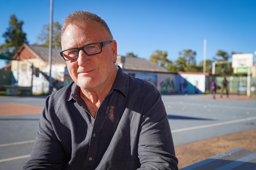A man sits at a table in front of a basketball court