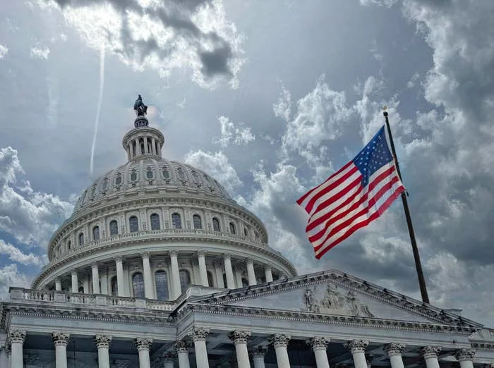 U.S. Capitol building with the American flag waving in the foreground under a cloudy sky