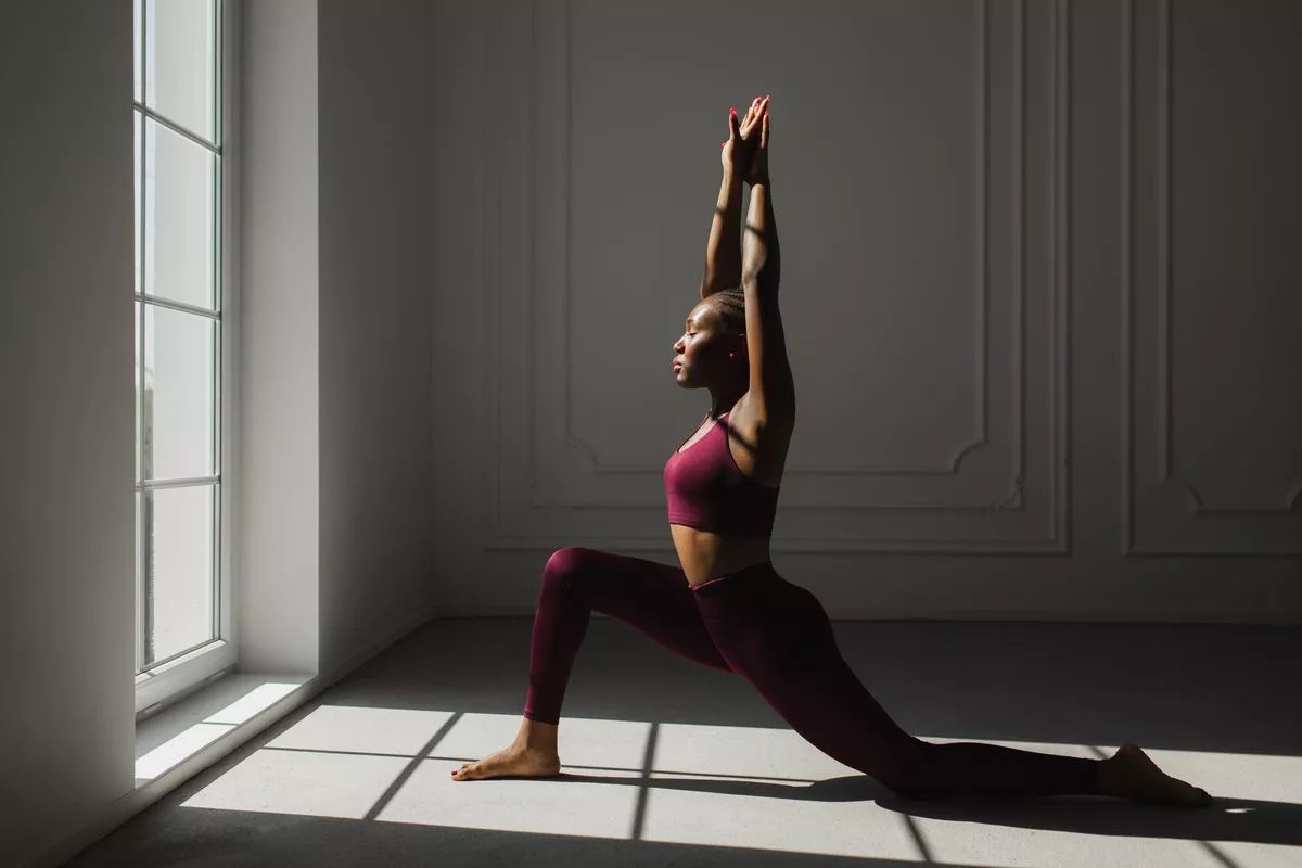 woman with braided hair practicing yoga and doing variation of High Lunge, version of Virabhadrasana I (Warrior I Pose).