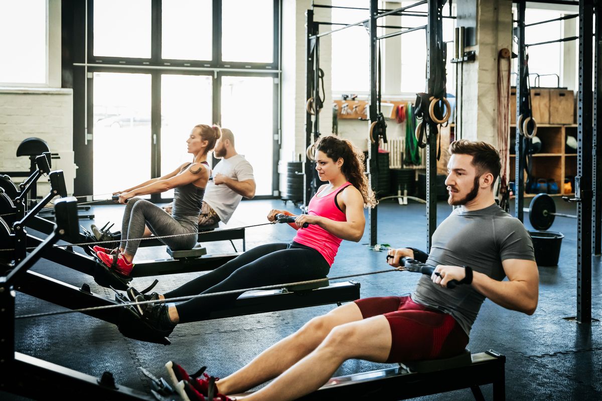 A group of fitness enthusiasts working out together at the gym using rowing machines - stock photo