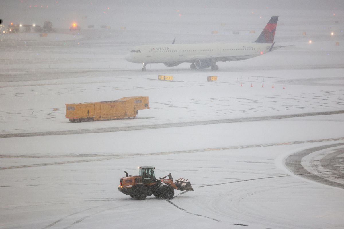 A snow removal machine is seen working while an Airbus A321 Delta Airlines taxied to take off on the tarmac of LaGuardia airport in New York on January 25