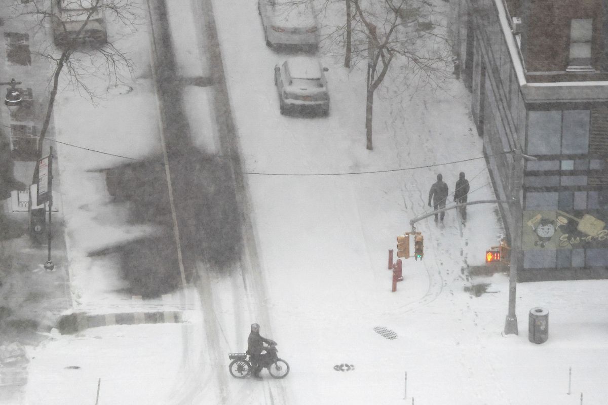 Pedestrians walk and ride their bike as heavy snow falls in New York