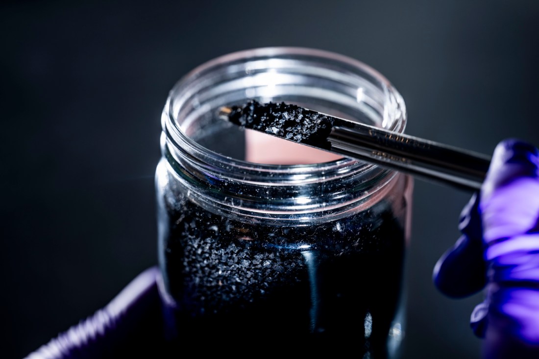 A small palette lifts particles of recycled tire rubber out of a glass jar.