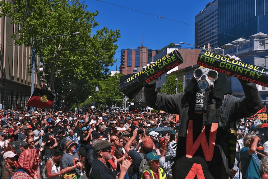 A man in a gas mask holding signs standing in front of a crowd on a road