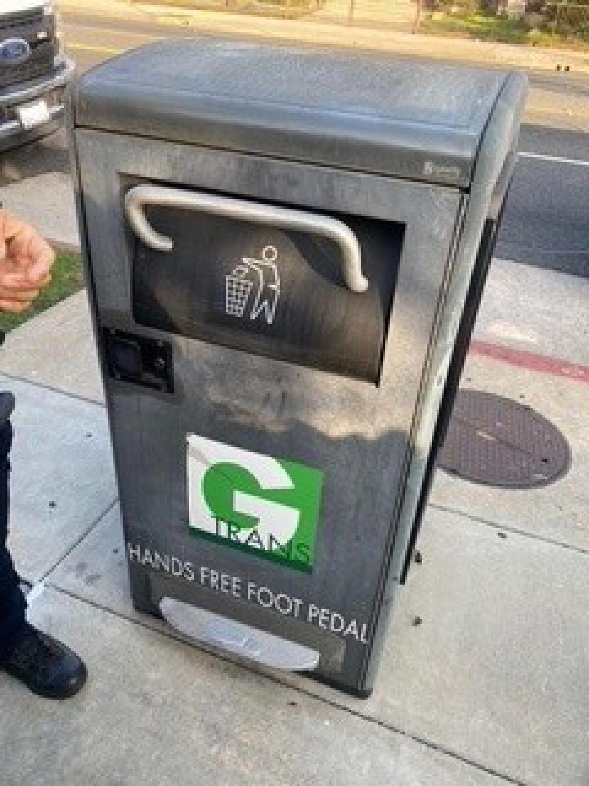 A metal trash can on a sidewalk.