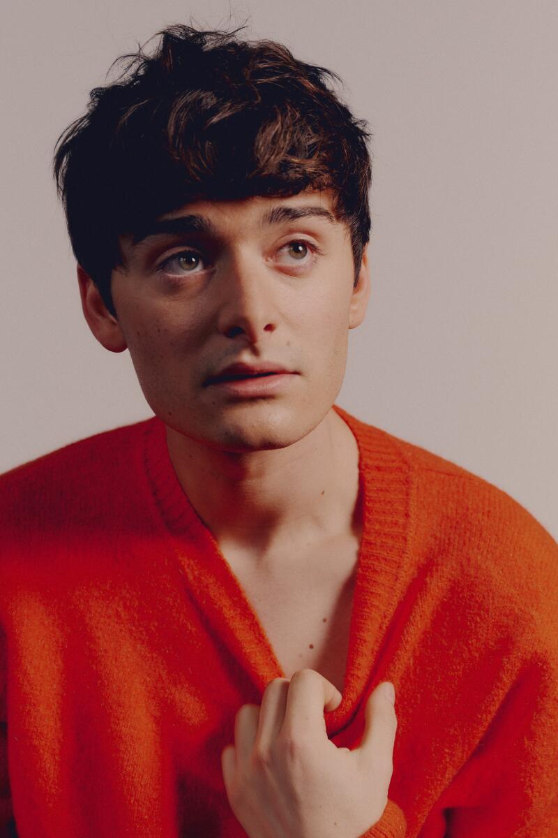 A young man stares into the distance while tugging on his orange sweater