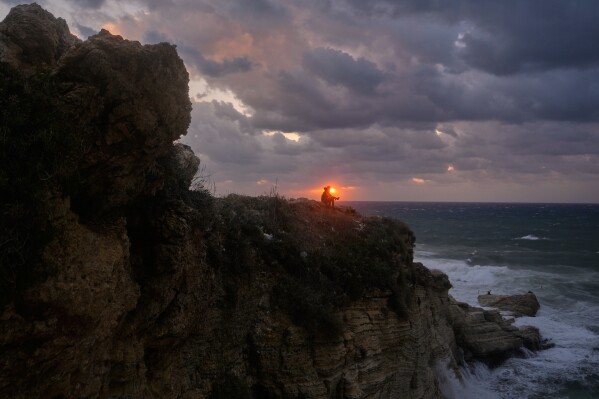 A man sits on a cliff as the last sunset of 2025 is seen over the Mediterranean Sea in Beirut, Lebanon, Wednesday, Dec. 31, 2025. (AP Photo/Hassan Ammar)