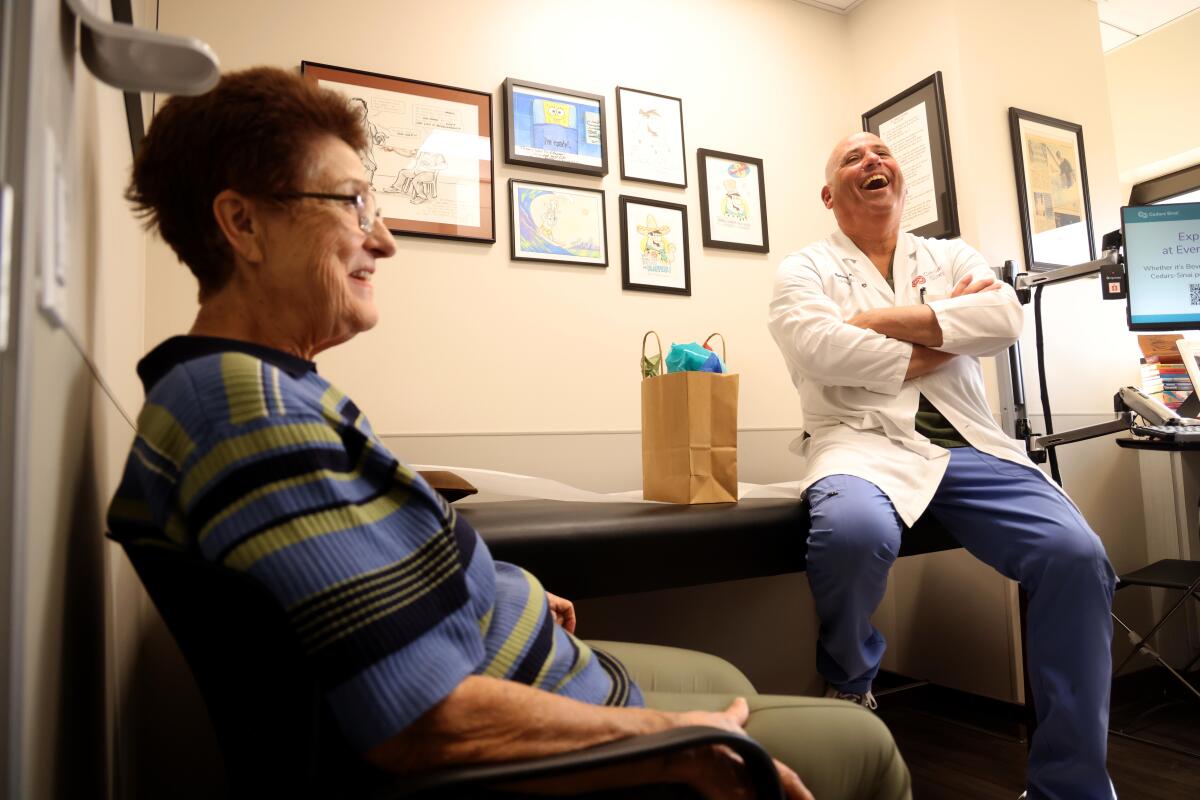 A woman is seated in a chair next to a man seated on a table.