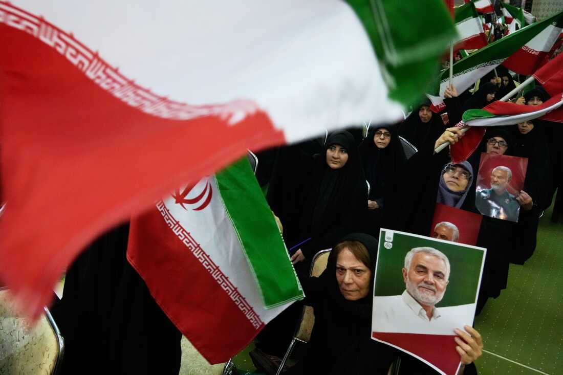 Women wave national flags as they hold up posters of the late commander of the Iran's Revolutionary Guard expeditionary Quds Force, Gen. Qassem Soleimani, who was killed in a U.S. drone attack in 2020 in Iraq, during a ceremony commemorating his death anniversary at the Imam Khomeini grand mosque in Tehran, Iran, on Thursday, Jan. 1.