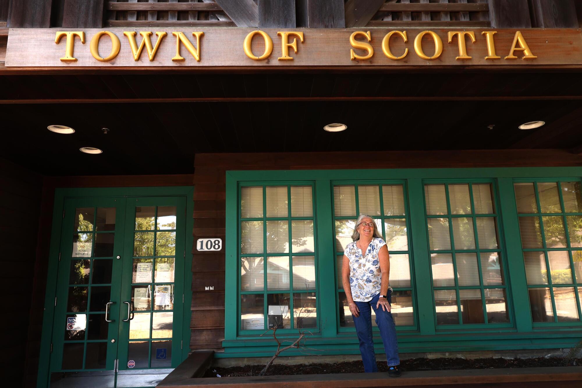 a woman stands on the street in front of a building with the words Town of Scotia written on it
