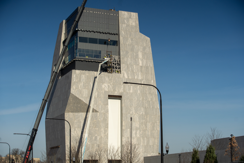 Workers install letters atop the 225-foot museum tower at the Obama Presidential Center.