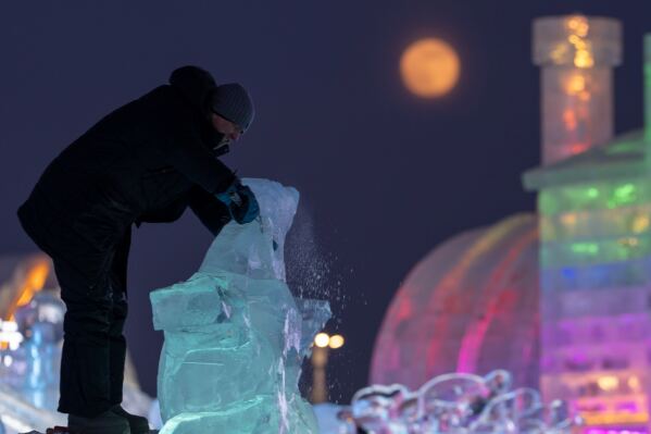 A ice sculptor prepares his work for competition as the Wolf Supermoon rises over the annual Ice and Snow Festival held in Harbin in northeastern China's Heilongjiang province on Saturday, Jan. 3, 2026. (AP Photo/Ng Han Guan)