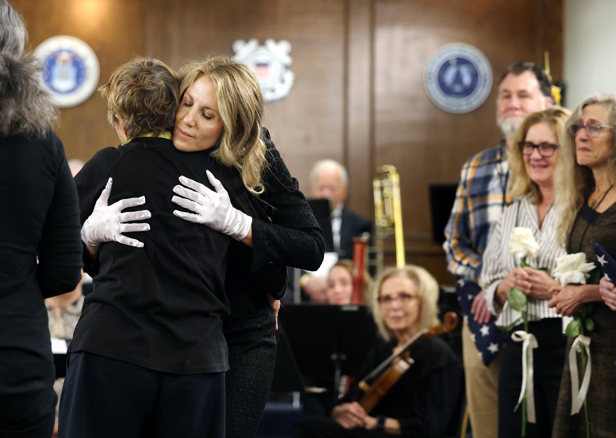 A woman in white gloves hugs another person as people look on.