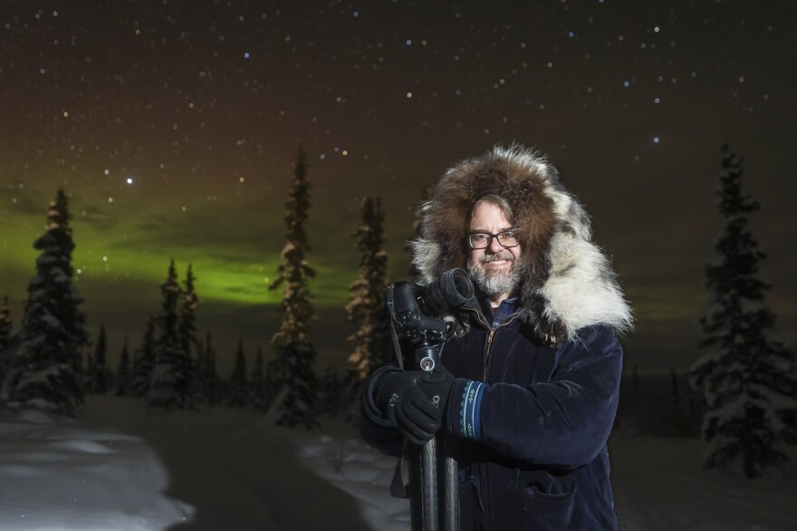 A man standing with a camera with the green aurora behind him
