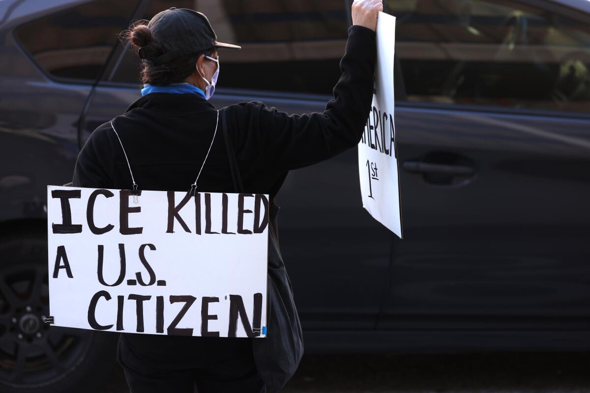A woman stands holding a poster reading 'ICE killed a U.S. citizen'
