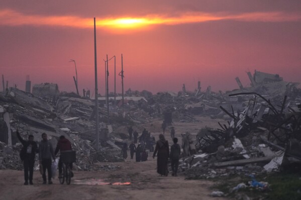 Palestinians walk through the ruins of destroyed buildings as the sun sets over Gaza City, Sunday, Jan. 4, 2026. (AP Photo/Jehad Alshrafi, File)