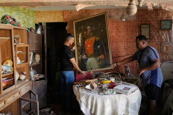 Jesus Linares, right, removes a painting of independence hero Simon Bolivar at his home, which he says was hit during U.S. military operations to capture Venezuelan President Nicolas Maduro, in Catia La Mar, Venezuela, Sunday, Jan. 4, 2026. (AP Photo/Matias Delacroix, File)