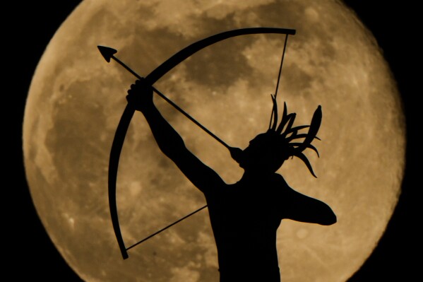 The full moon rises behind the statue, "Ad Astra," atop the Kansas Statehouse, Saturday, Jan. 3, 2026, in Topeka, Kan. (AP Photo/Charlie Riedel, File)
