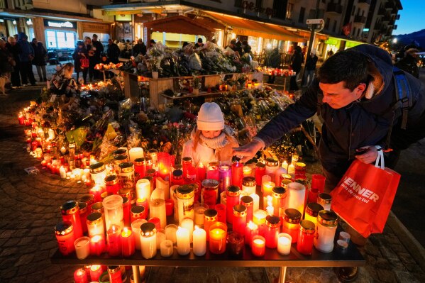 A child watches as an adult places a candle outside the sealed off Le Constellation bar in Crans-Montana, Swiss Alps, Switzerland, Saturday, Jan. 3, 2026, where a devastating fire left dead and injured during the New Year's celebrations. (AP Photo/Baz Ratner, File)