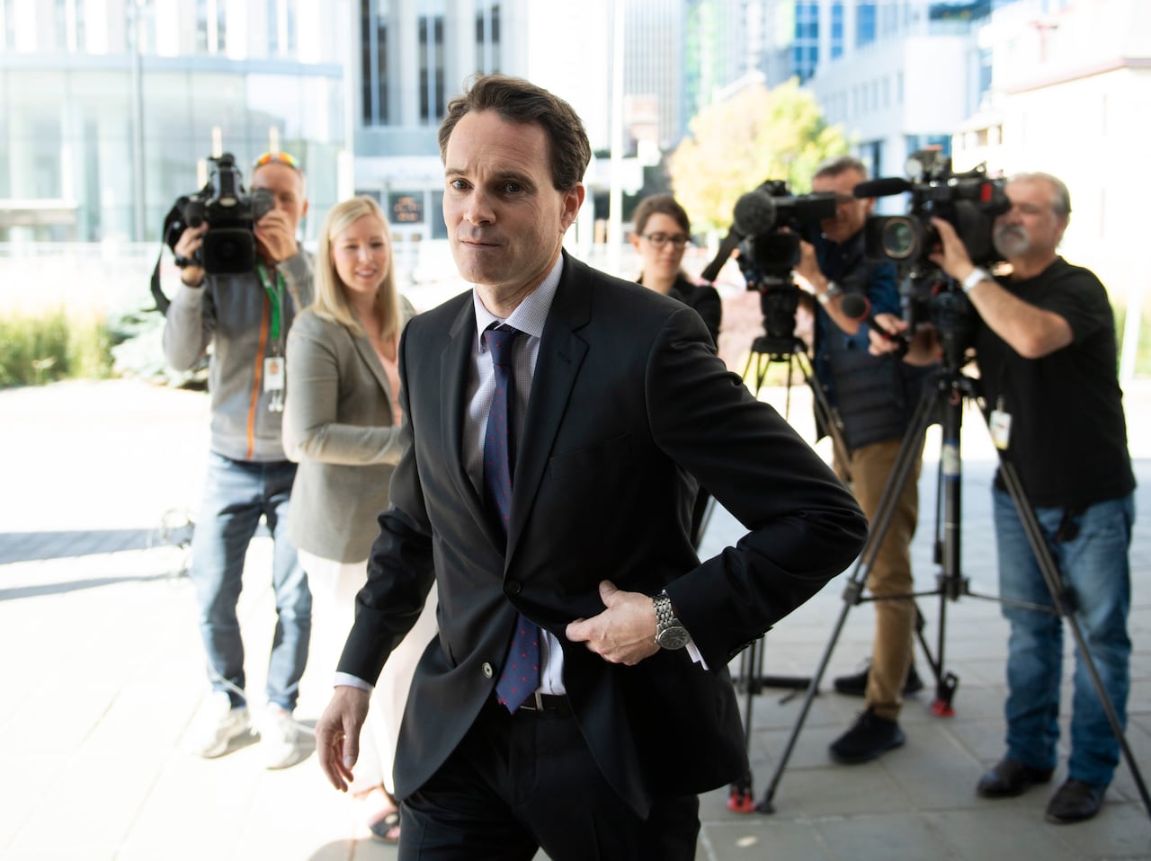 A man in a suit outside a courthouse in front of a crowd of reporters.