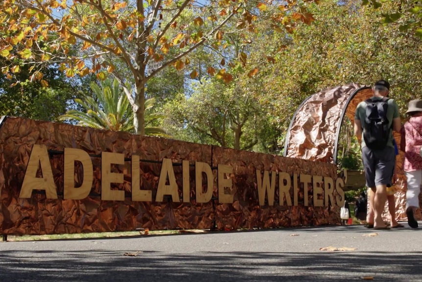 A sign saying "Adelaide Writers Week" in front of a park.