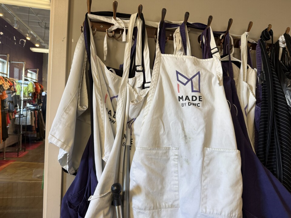 A bunch of candlemakers' aprons hanging on the wall. A white apron in front of the pile is adorned with the Made by DWC logo. 