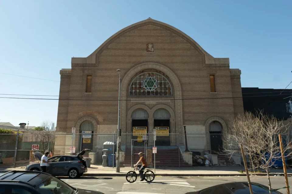 A large brown building gated off from street entrance with cars parked in front.
