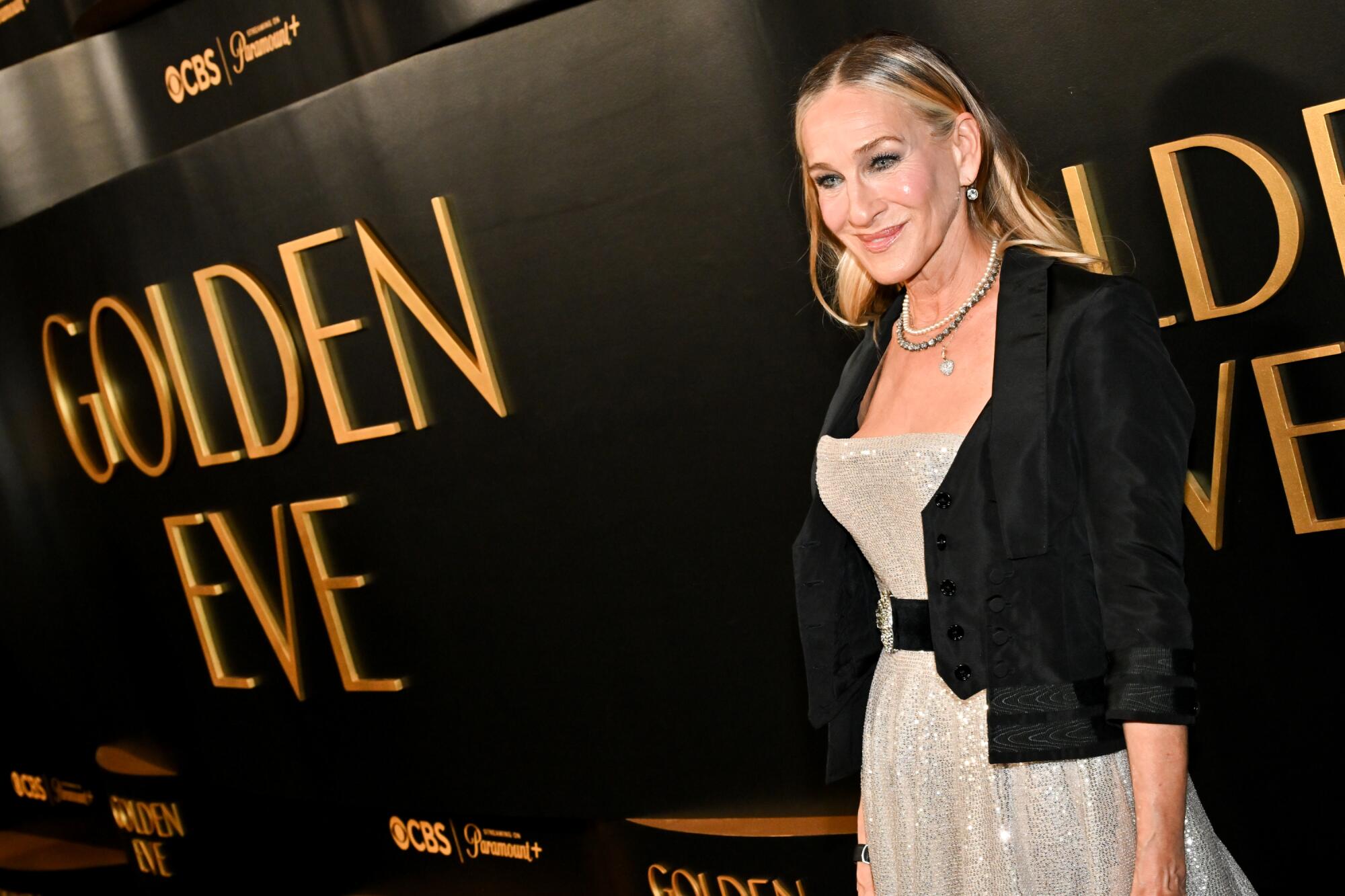 Sarah Jessica Parker, in a sequin dress and black blazer, smiles at cameras.
