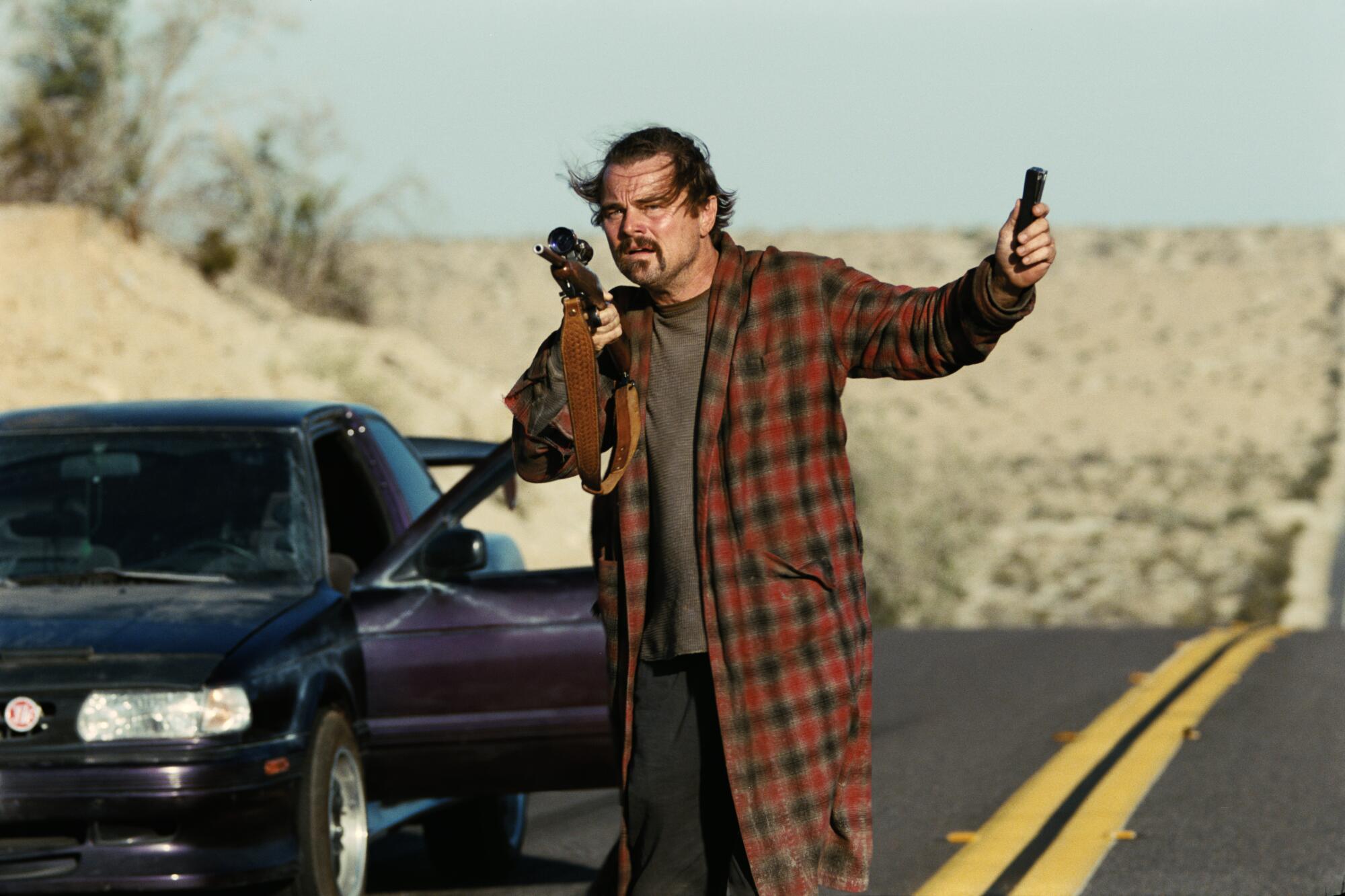 A man in a bathrobe stands on a desert road.