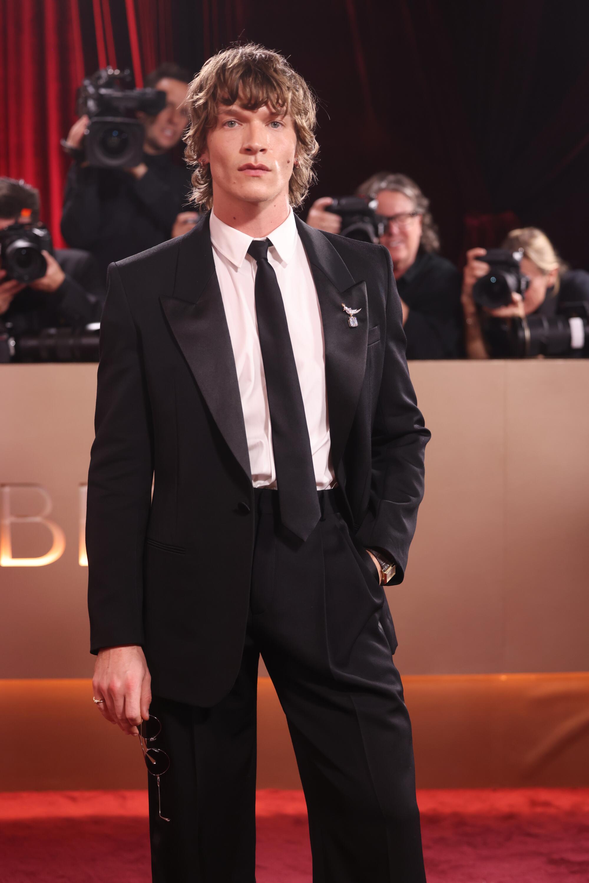 Connor Storrie, in a black suit and tie, poses on the red carpet. 