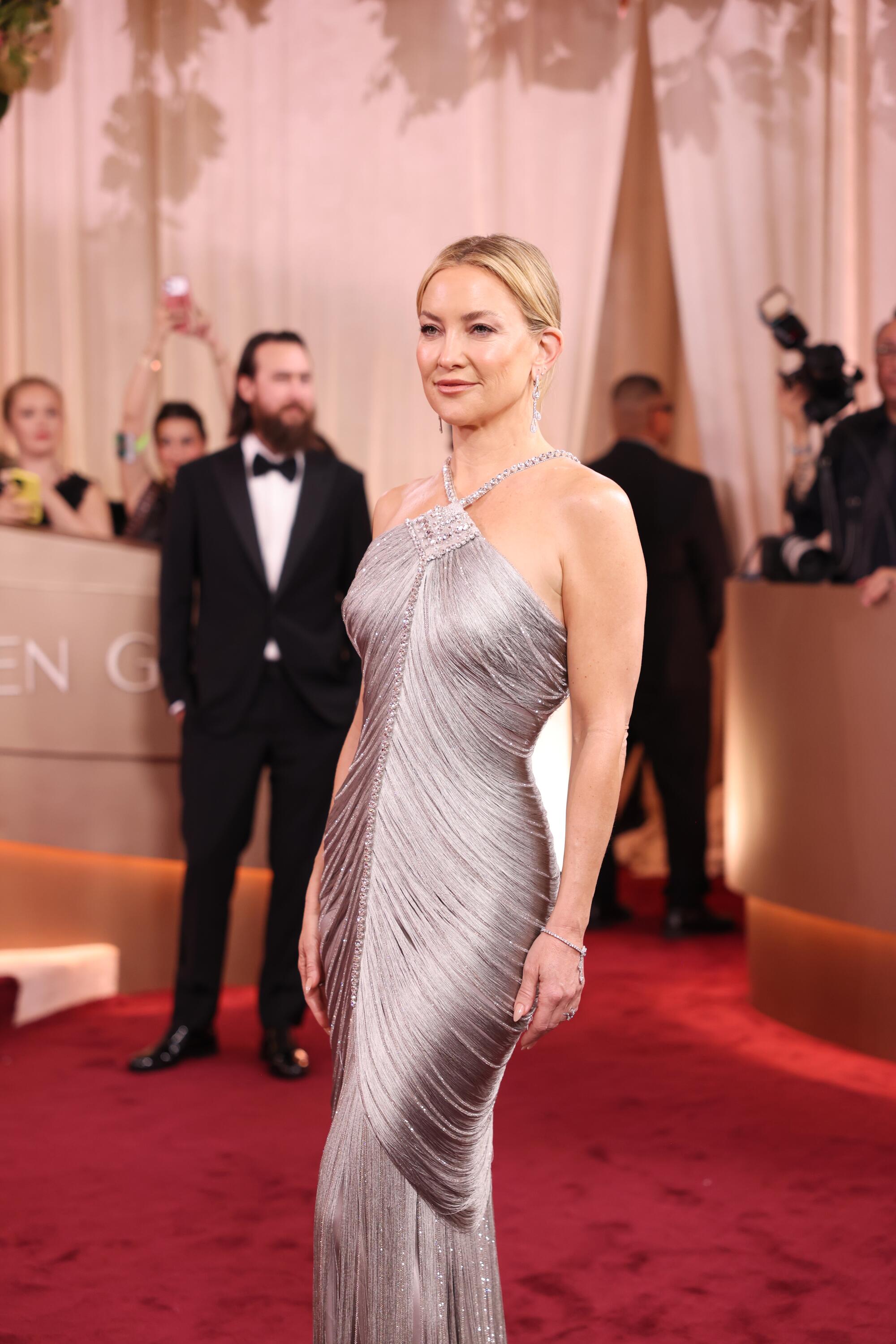 Kate Hudson, in a silver gown, walks the red carpet. 